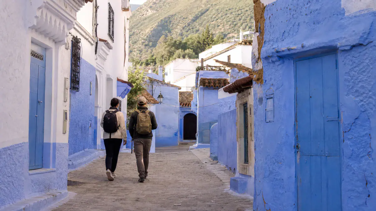 Travelers walking into Chefchaouen's blue medina below the Rif Mountains