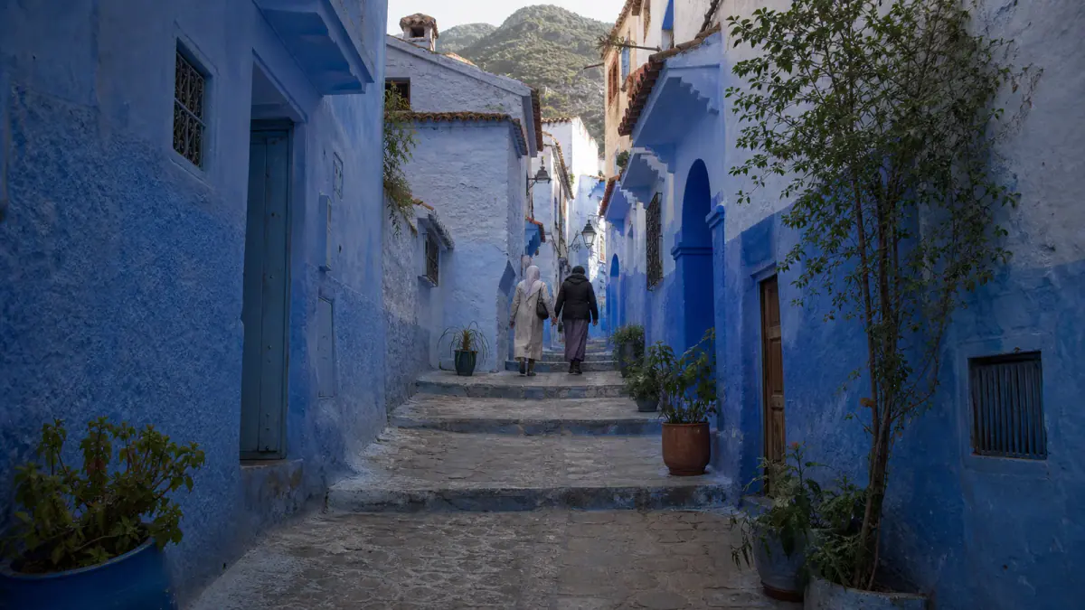 Travelers walking respectfully through a quiet blue stepped lane in Chefchaouen's hillside medina