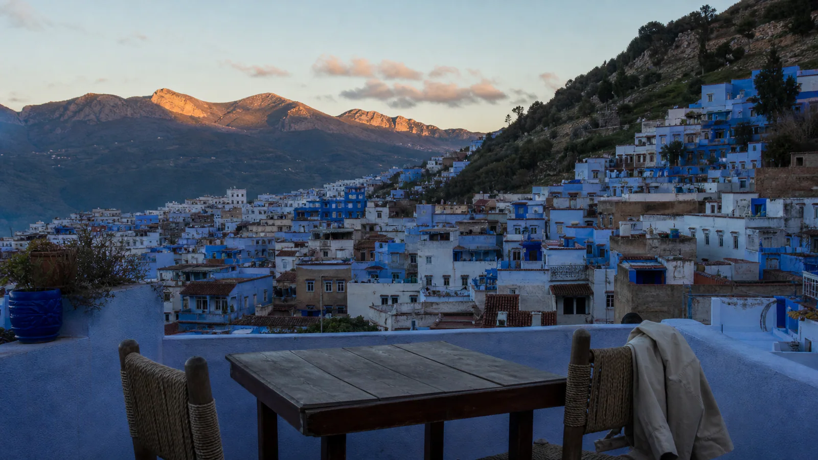 Chefchaouen medina and Rif Mountains seen from a quiet guesthouse rooftop at dusk