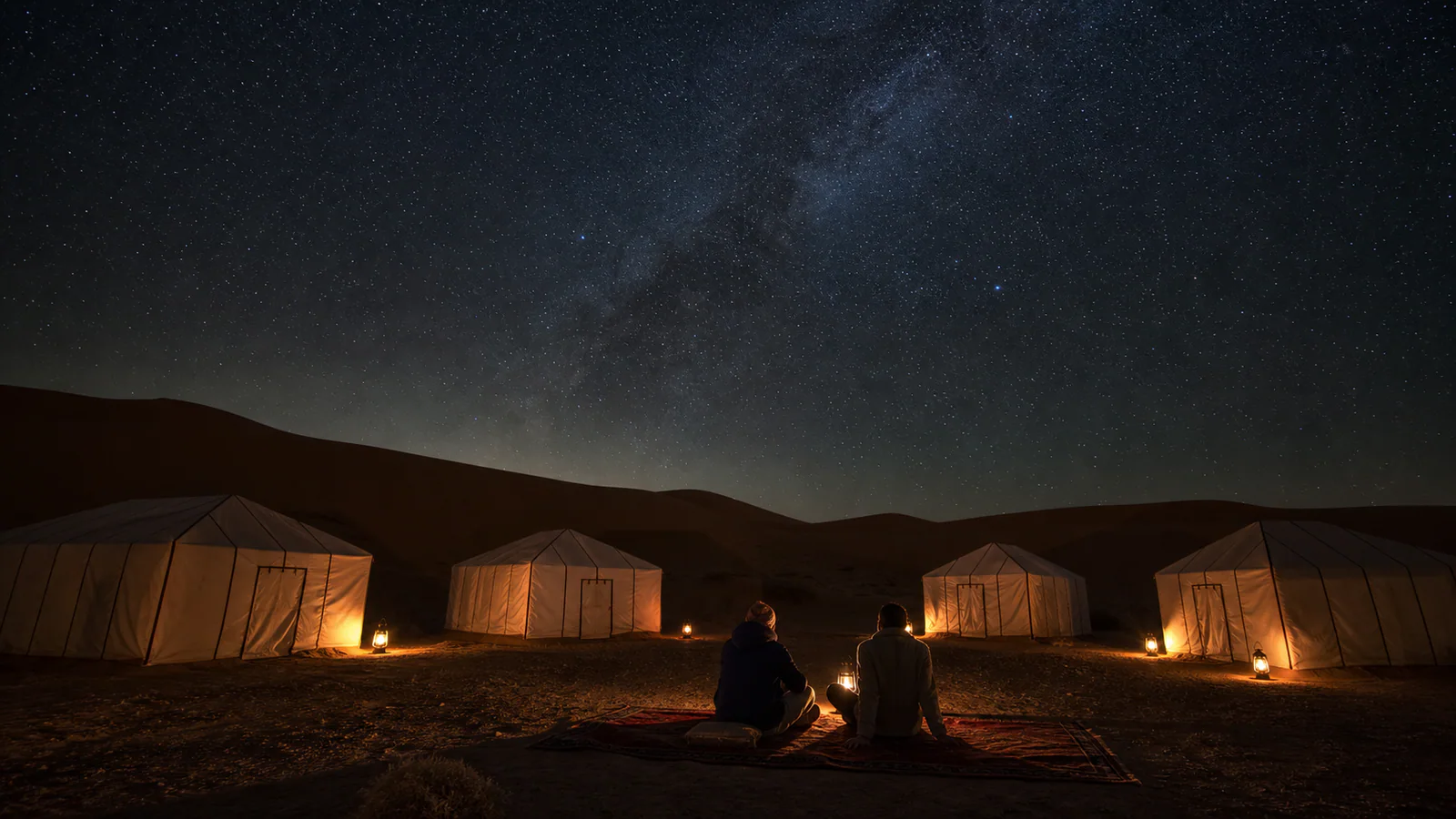 Travelers watching a realistic night sky from a small camp near the Merzouga dunes