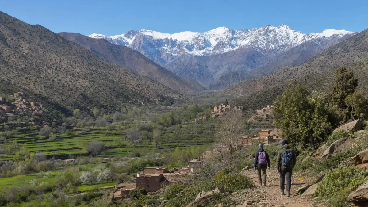 Spring hikers overlooking a green Atlas valley with snow on distant peaks