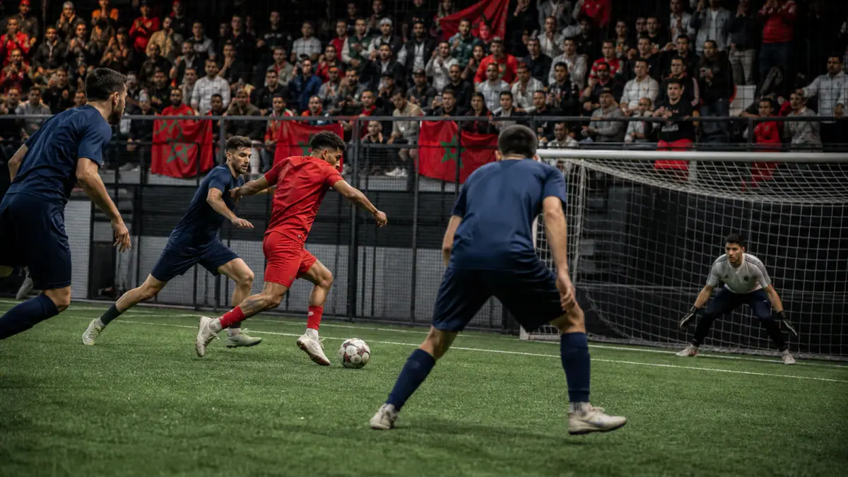 Red-kit Moroccan attacker under pressure near goal in a compact indoor football arena
